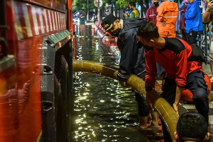 Petugas armada mobil pompa Dinas Pemadam Kebakaran dan Penyelamatan (DPKP) menyedot genangan air banjir.