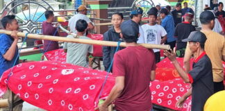 Warga Desa Pagerngumbuk Sidoarjo mengarak tumpeng dan hasil bumi di atas amben bambu saat tradisi ruwat desa.